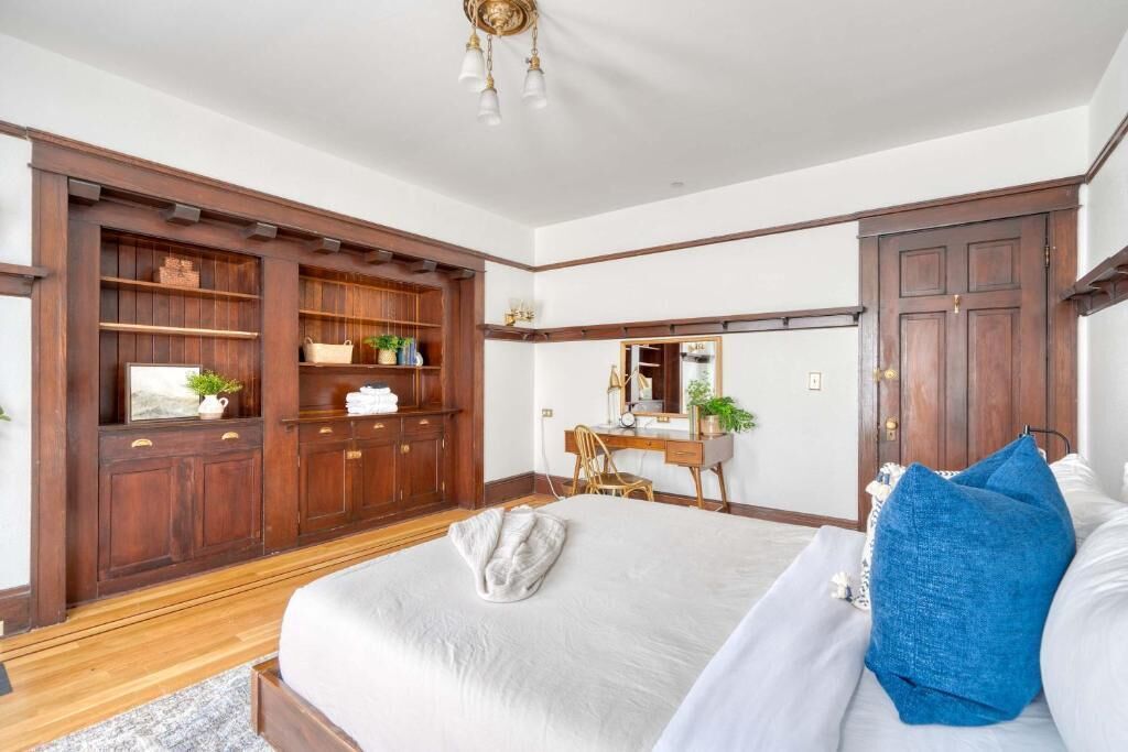 Un dormitorio con una cama grande, un armario de madera, un escritorio con silla y un espejo.