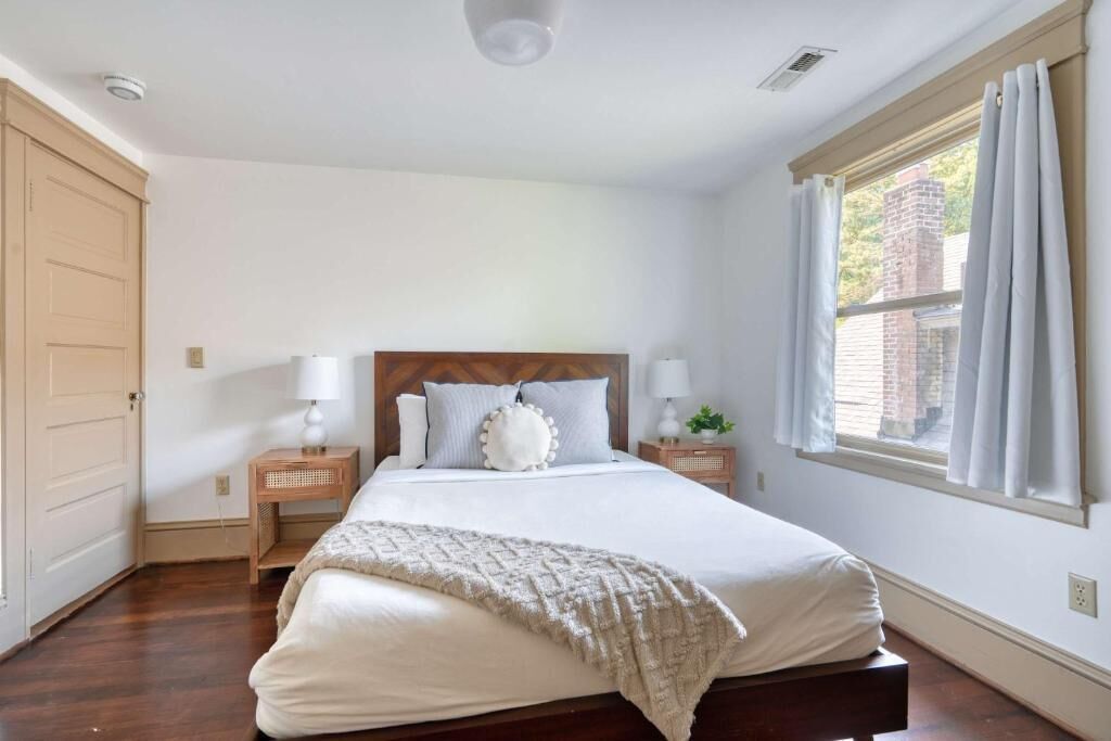 Un dormitorio con una cama de madera, dos mesitas de noche, una ventana con cortinas y una puerta.