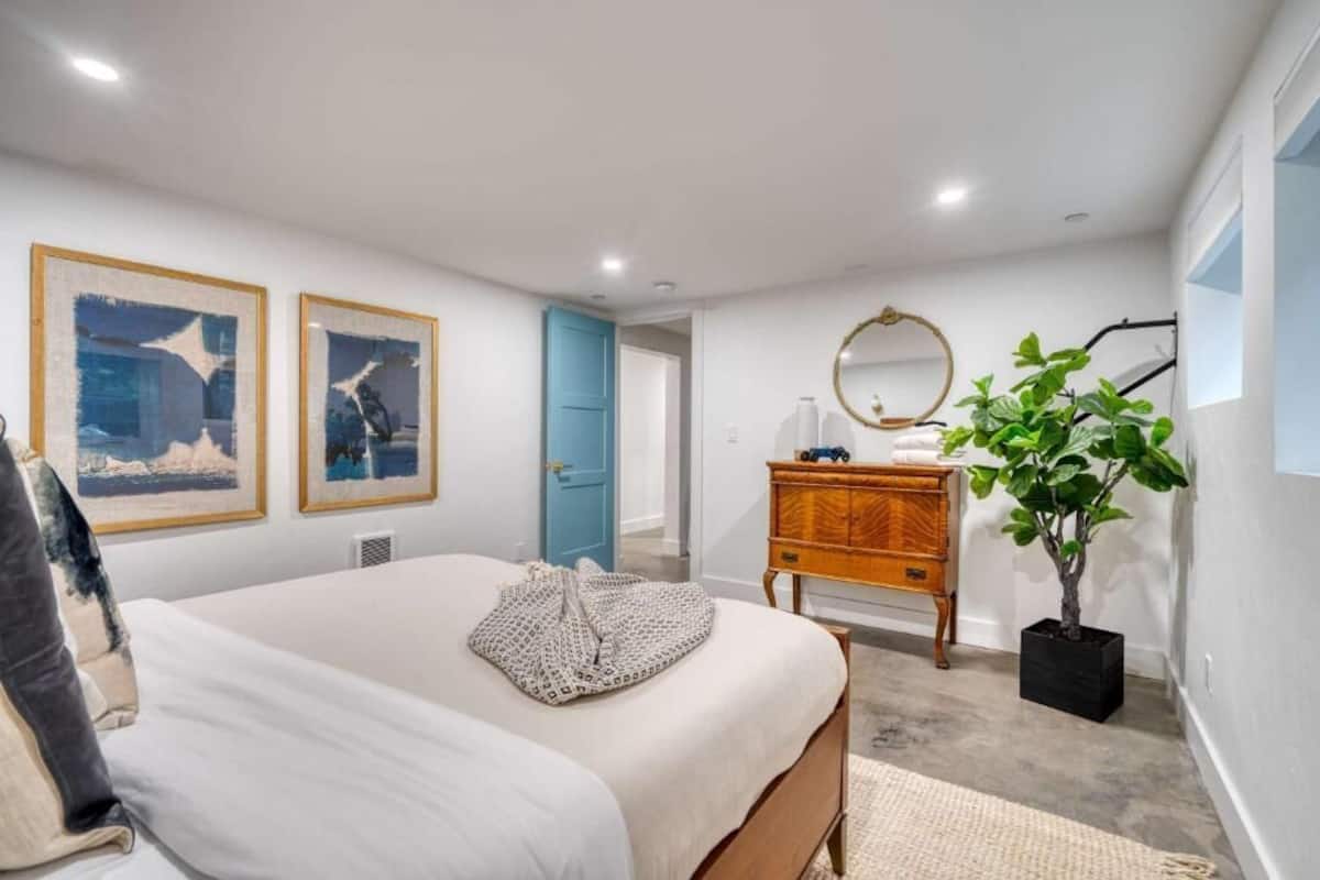 A bedroom with a bed, two framed pictures, a dresser, a mirror, and a potted plant.
