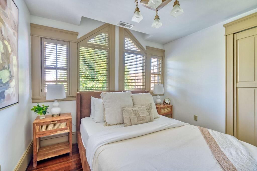 A bedroom with a large bed, two bedside tables with lamps, a window with blinds, and a ceiling fan.