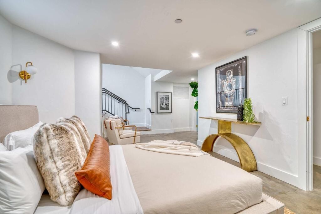 A bedroom with a bed, a nightstand, a chair, a staircase, and a wall-mounted shelf with a plant.