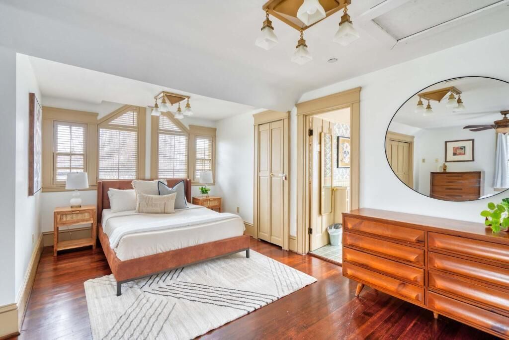 Une chambre à coucher avec un lit, une commode, un miroir et un plancher en bois.