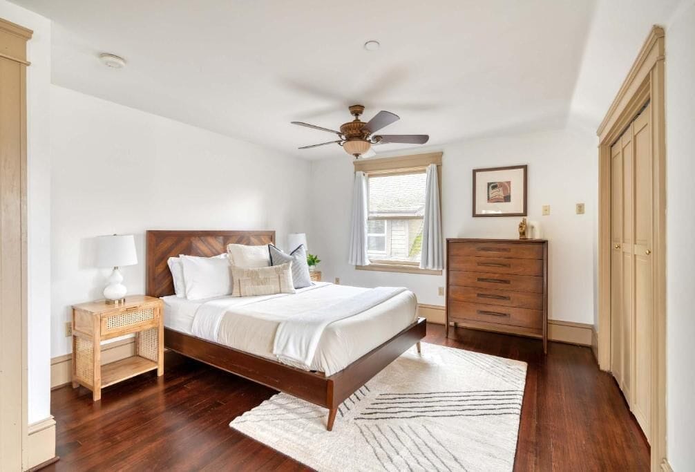 A bedroom with a bed, a nightstand, a dresser, a ceiling fan, and a window.
