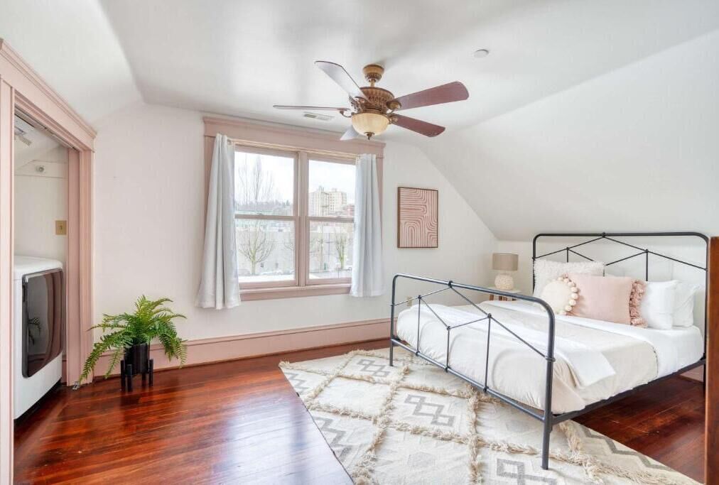 A bedroom with a bed, a ceiling fan, a window, and a plant.
