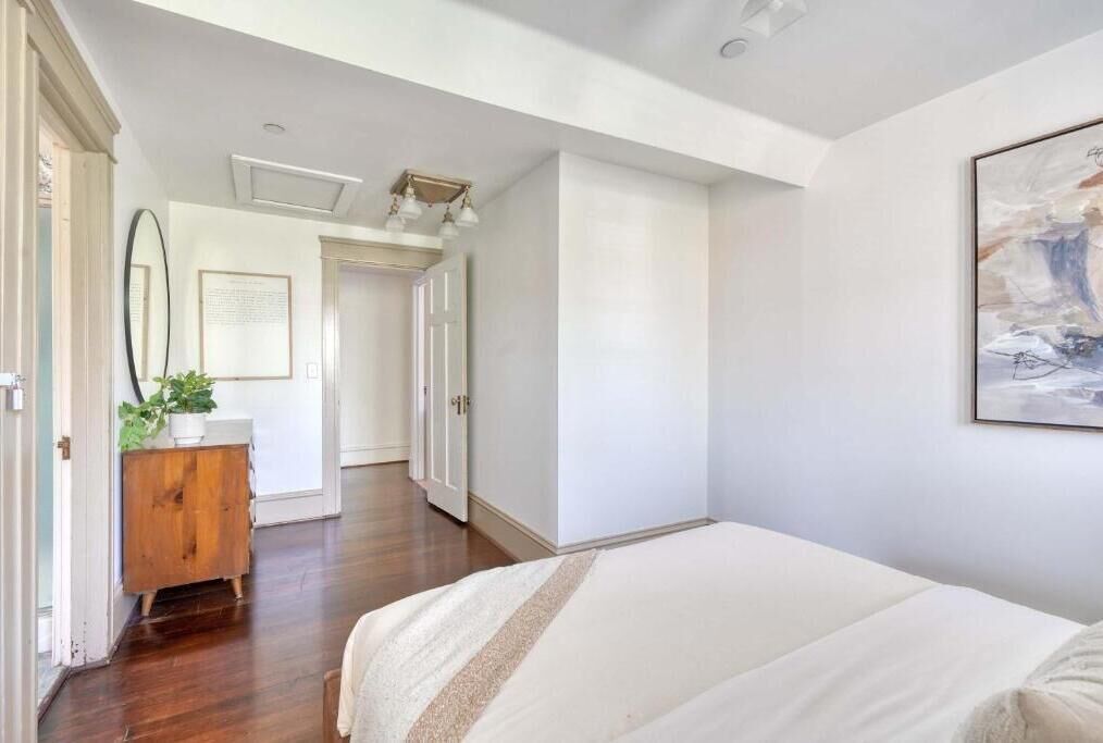 A bedroom with a bed, a wooden dresser, a mirror, and a framed picture on the wall.