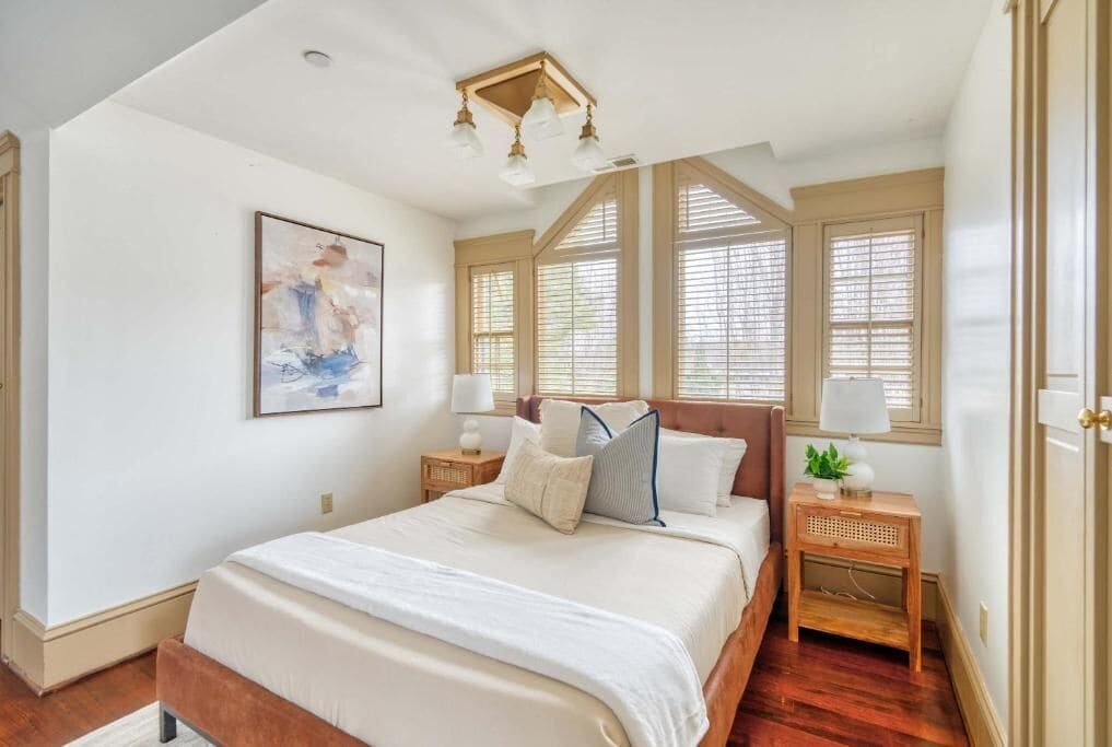 A bedroom with a large bed, a ceiling light fixture, and a window with blinds.