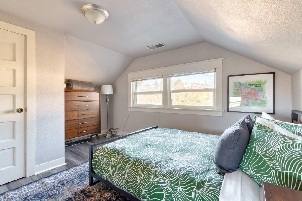 A bedroom with a bed, dresser, lamp, window, and a framed map on the wall.