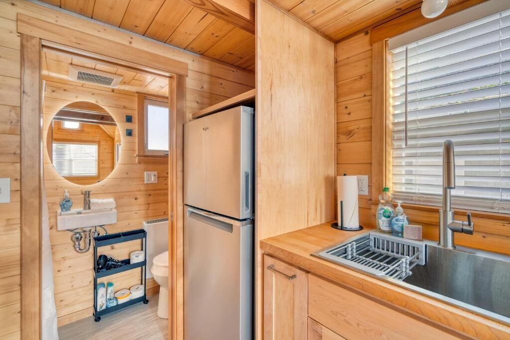 Una cocina compacta con paredes de madera, un refrigerador, un lavamanos y una ventana con persianas.