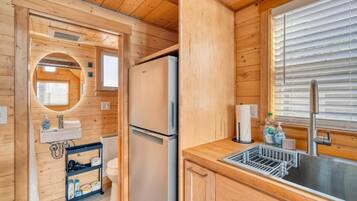Una cocina compacta con paredes de madera, un refrigerador, un lavamanos y una ventana con persianas.
