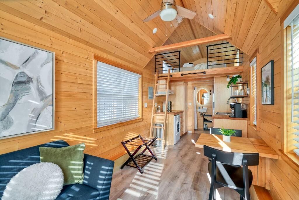 A wooden cabin interior with a dining area, kitchen, and a loft bedroom.