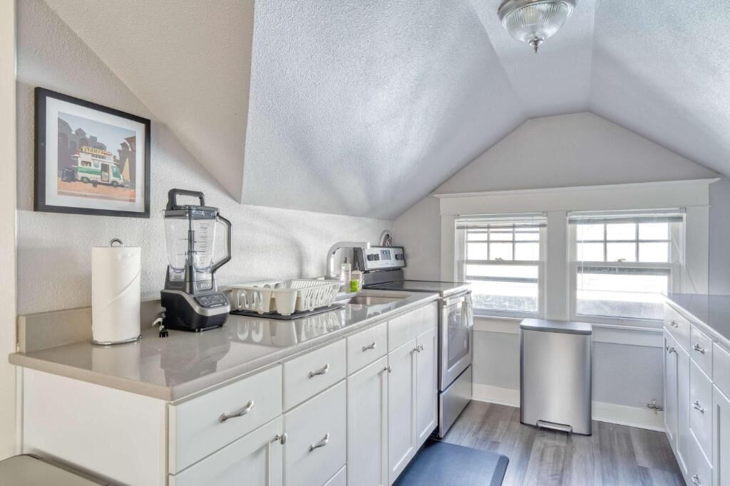Een moderne keuken met een aanrecht, een spoelbak en een prullenbak. Er hangt een lijst met een afbeelding aan de muur.