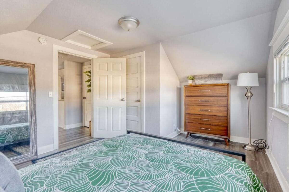 A bedroom with a bed, a dresser, a lamp, and a door leading to another room.