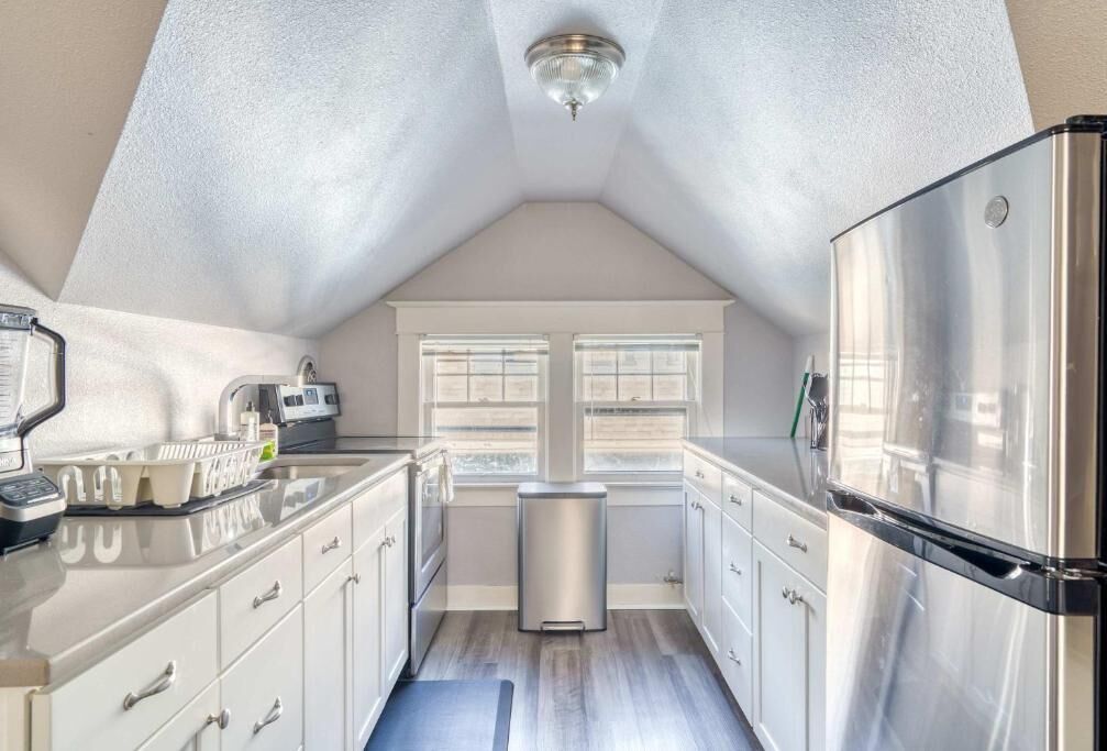 A modern kitchen with a stainless steel refrigerator, a built-in oven, and a window with blinds.