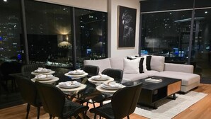 A modern living room with a dining area, large windows with city views, and a white sofa. - Charming 2-bedroom Apartment in Central Melbourne (Melbourne)