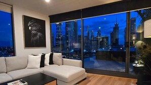 A modern living room with a large window, a sofa, a coffee table, and a cityscape view. - Charming 2-bedroom Apartment in Central Melbourne (Melbourne)