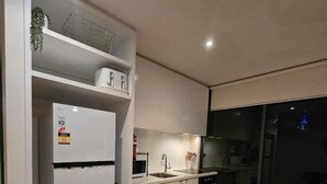 A modern kitchen with white cabinetry, a built-in microwave, and a dining area with a round table. - Charming 2-bedroom Apartment in Central Melbourne (Melbourne)