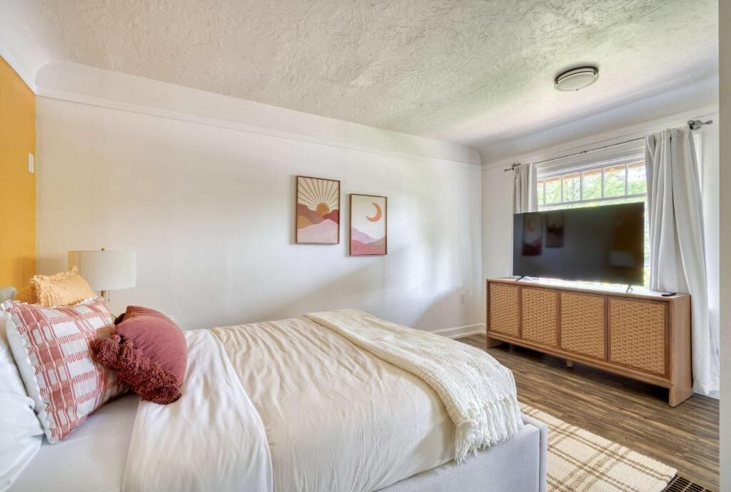 Une chambre à coucher comprenant un lit, un téléviseur, une fenêtre avec des rideaux et un meuble fixé au mur.