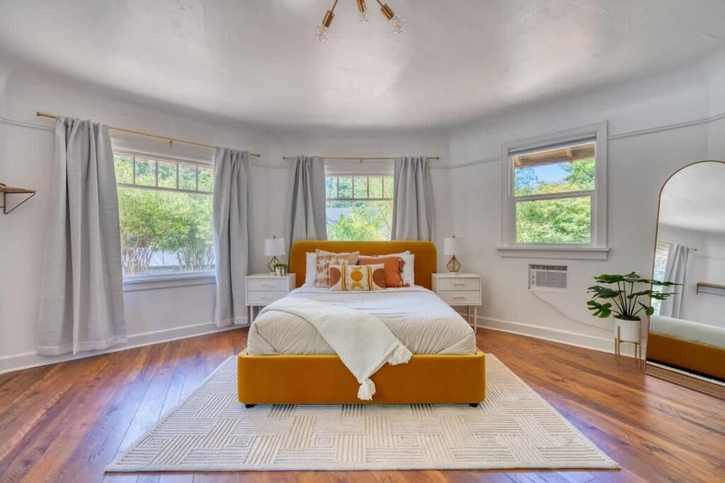 A bedroom with a bed, two bedside tables, a nightstand, a window, and a plant.
