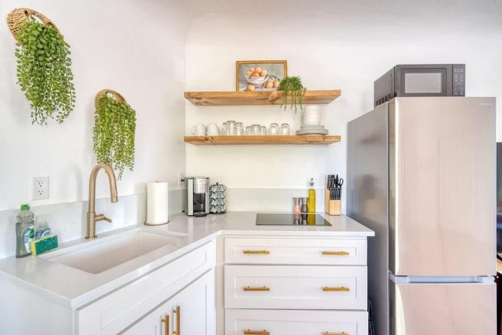 A kitchen with white cabinets, a stainless steel refrigerator, hanging plants, and a coffee maker.