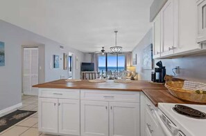 A kitchen with white cabinets, a wooden countertop, a stove, and a view of the ocean. - Seaside Beach & Racquet Club 3503 | Beachfront, Pools, Tennis, Fitness | Beach Getaways (Orange Beach)