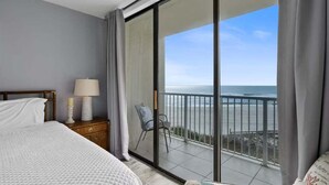 Ein Schlafzimmer mit einer großen Glasschiebetür, die auf einen Balkon mit Meerblick führt.
