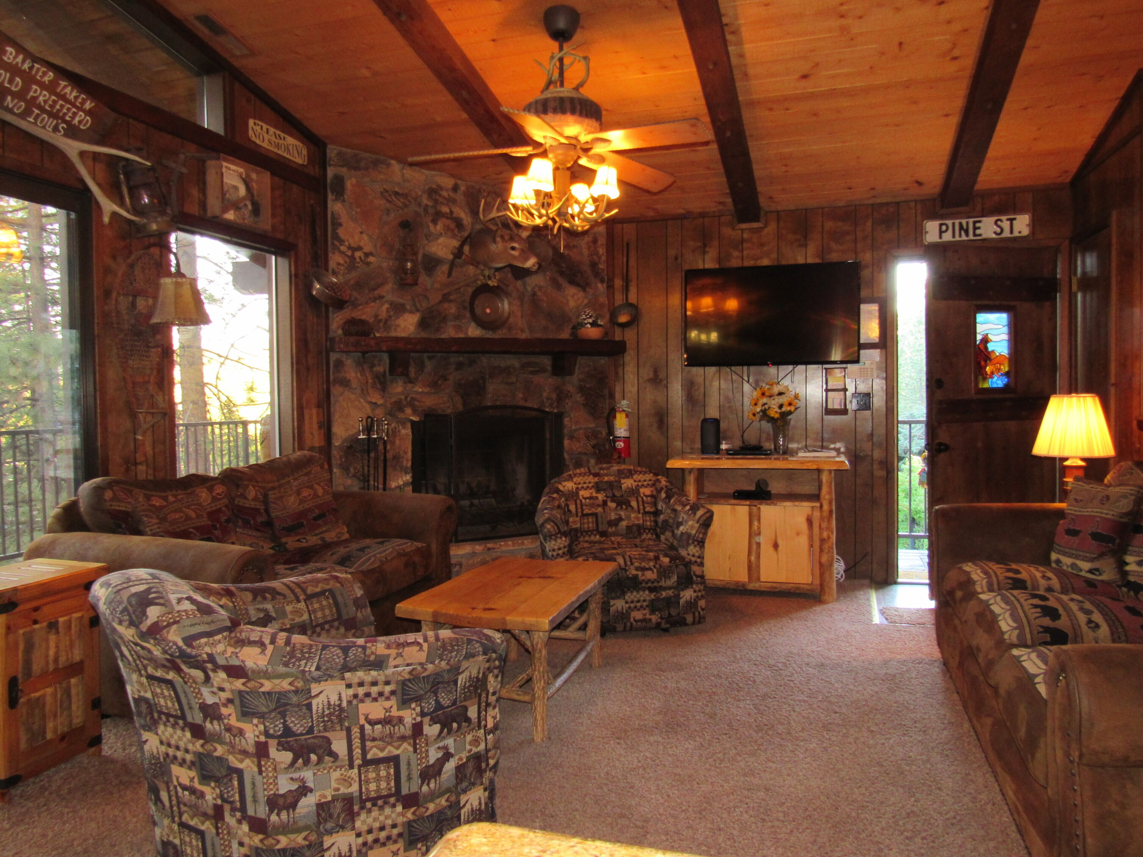 A rustic interior with a stone fireplace, wooden furniture, a television, and a sign reading 'Pine St.'