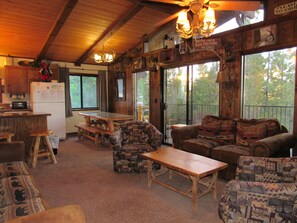 Ein rustikales Cabin-Interieur mit Holzmöbeln, einem Esstisch, einem Kühlschrank und einem großen Fenster mit Blick ins Freie.