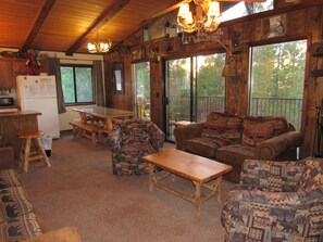 Ein rustikales Cabin-Interieur mit einem Holzespeisetisch, zwei gemusterten Sofas, einer Holzbank und einem Kühlschrank.
