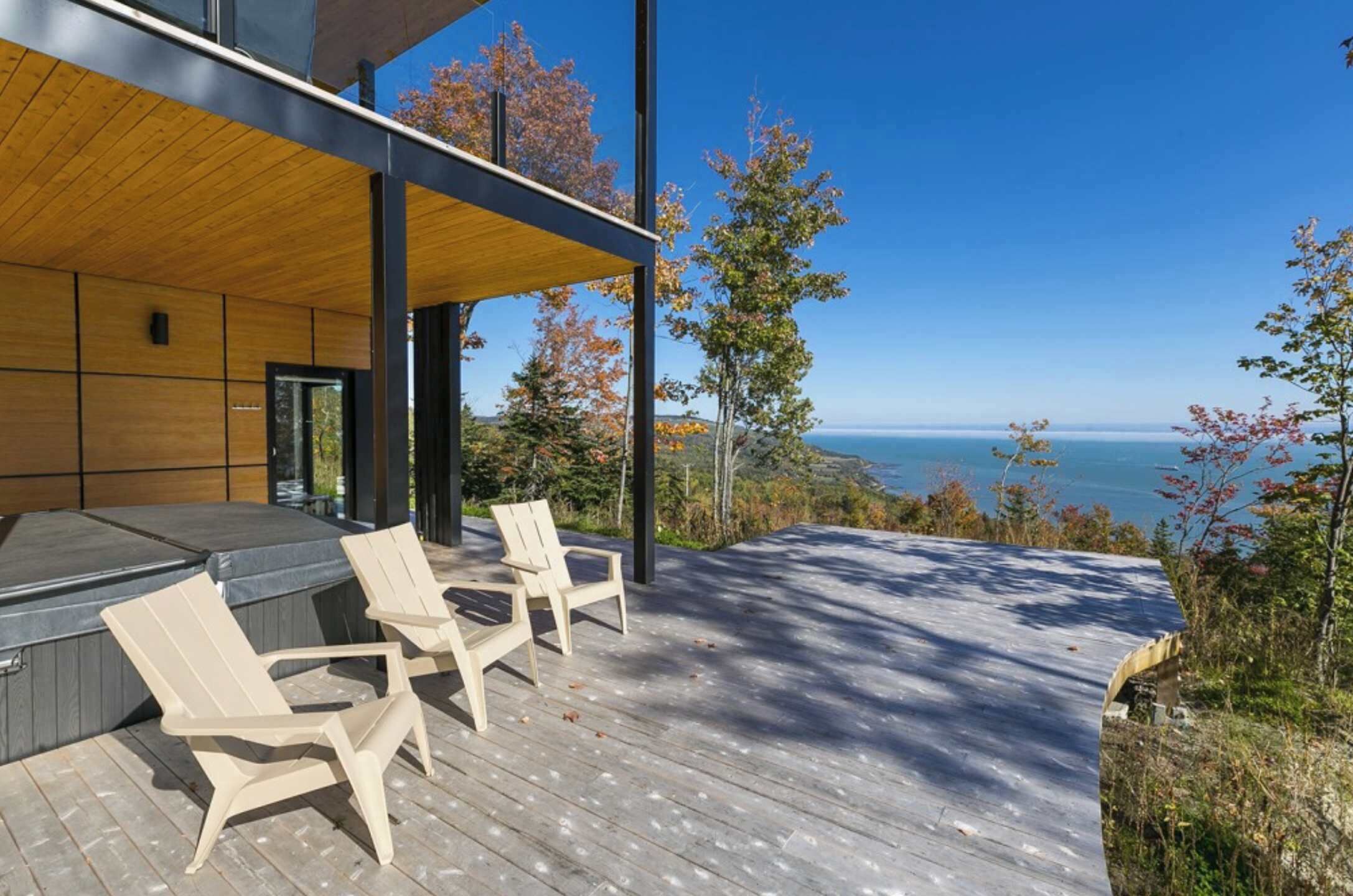 Eine moderne Terrassenanlage im Freien mit Holzboden, einem Whirlpool und zwei Adirondack-Stühlen.