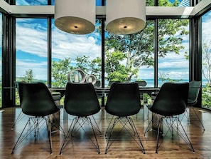 A modern dining area with a table set for four, large windows, and a view of trees and sky.
