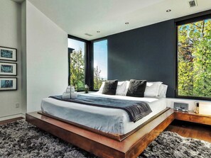 Ein modernes Schlafzimmer mit einem großen Bett, Blick auf Bäume und einer dunklen Akzentwand.
