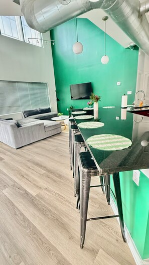 A modern kitchen with a green accent wall, a dining area with stools, and a sofa in the background. - Spacious 3/3 bedrooms- Walk to Eats, Shops and Entertainment (Atlanta)
