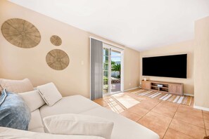 Ein Wohnzimmer mit einer Couch, einem Flachbildfernseher und einer Schiebeglastür, die auf eine Terrasse führt.
