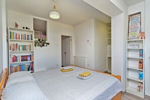 A bedroom with a bed, a bookshelf, a radiator, and a door leading to another room. - Holiday apartment with air conditioning and washing machine (Pula)