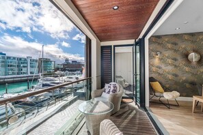 A balcony with wicker furniture, a glass table, and a view of a marina. - Gorgeous 2-Bed 2-Bath Harbour View Stunner (Auckland City)