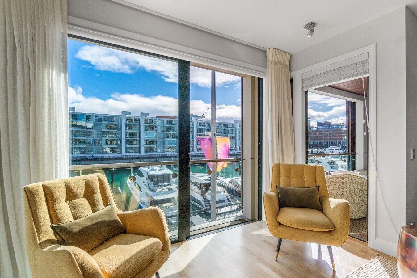 A modern living room with large windows, a sofa, a chair, and a view of a marina and buildings.