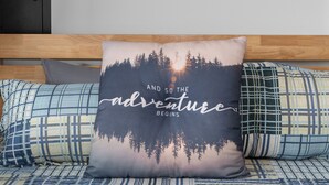 Makuuhuone, jossa on sänky, metsä- ja auringonlaskukuviollinen tyyny sekä maalaus veneistä, joka on tehty puiseen seinään.