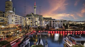 A waterfront cityscape with modern buildings, a prominent tower, and a marina with boats. - Luxury 2-Bed Marina Apartment Pool, Spa & Gym (Auckland City)