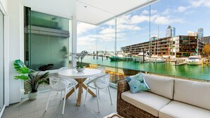 A balcony with a dining table, chairs, a sofa, and a view of a marina with boats and buildings. - Luxury 2-Bed Marina Apartment Pool, Spa & Gym (Auckland City)