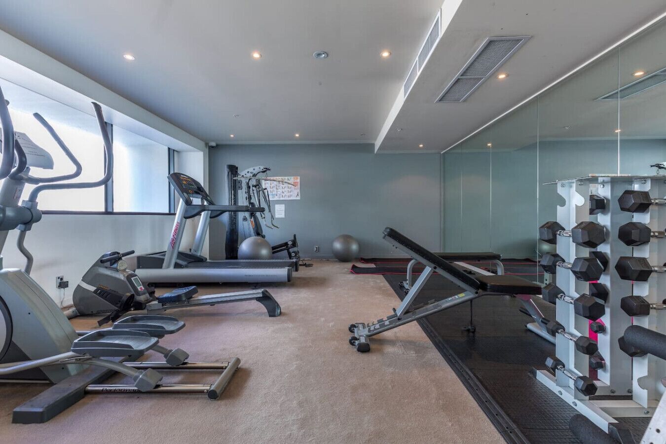 Un gimnasio con máquinas de cardio, pesas libres y un espejo grande.