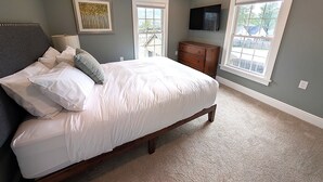 A bedroom with a bed, a dresser, a TV mounted on the wall, and a window.