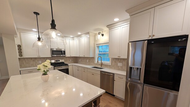 A modern kitchen with white cabinets, stainless steel appliances, a marble countertop, and pendant lighting.
