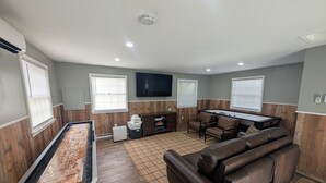 A pool table, a sofa, a television, and a ping pong table in a room with wooden paneling and a tiled floor.