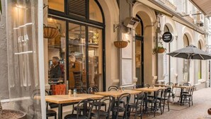 En udendørs café med borde, stole og en glasfacade, samt et skilt med teksten 'KELBA'.