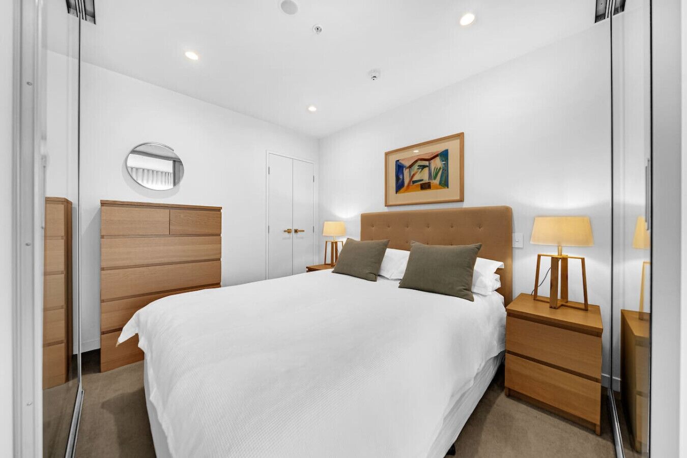A bedroom with a large bed, bedside tables, a wardrobe, and a painting on the wall.