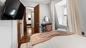 Un dormitorio con cama, escritorio, silla, televisor y ventana con cortinas.