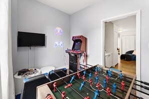 A room with a foosball table, a flat-screen TV, and a retro arcade machine. - LUX 4BR Somerville, Steps to Green Line, Free Parking, Game Room+Poker Table (Somerville)