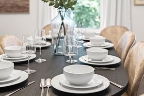 Una mesa de comedor preparada con platos, tazones y copas de vino, rodeada de sillas.