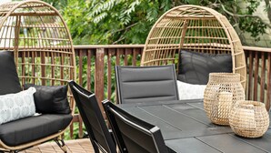 Una silla de mimbre con cojín, una mesa con sillas y una cesta de mimbre en una terraza.