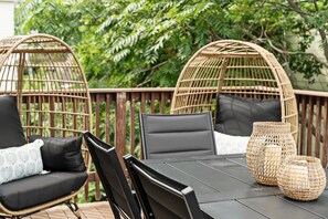 Una silla de mimbre con cojín, una mesa con sillas y una cesta de mimbre en una terraza.